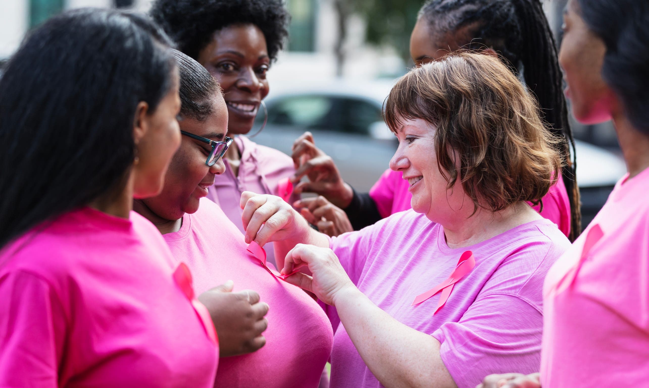 Women in pink T-shirts, one wearing a pink ribbon, smiling together